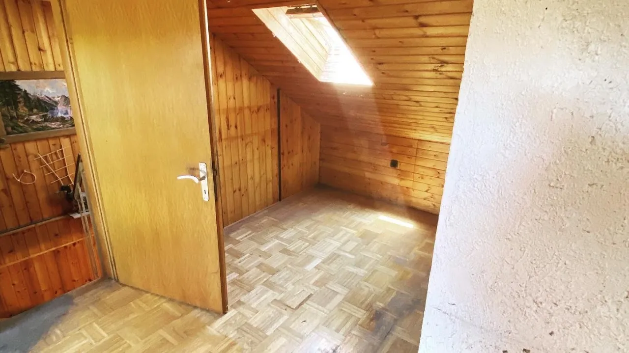 Leeres Dachzimmer mit Parkett und Dachfenster, bereit zum Renovieren