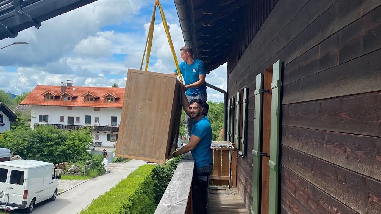 Zwei Mitarbeiter von SM Team heben einen Schrank mit einem Kran über den Balkon eines Bauernhauses