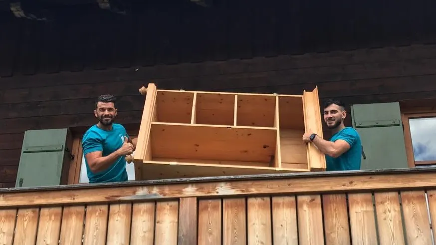 Zwei Mitarbeiter heben ein Holzregal über die Brüstung eines Balkons